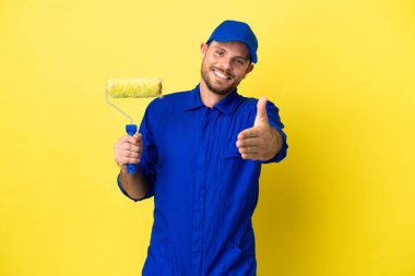 Ressam Brezilyalı izole edilmiş sarı arka planda iyi bir anlaşma için el sıkışıyor.