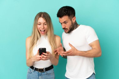 İzole edilmiş mavi arkaplan üzerinde genç bir çift cep telefonuyla bir mesaj veya e-posta gönderiyor