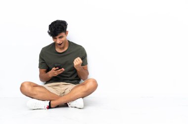 Yerde oturan genç Arjantinli adam şaşırdı ve bir mesaj gönderiyor.