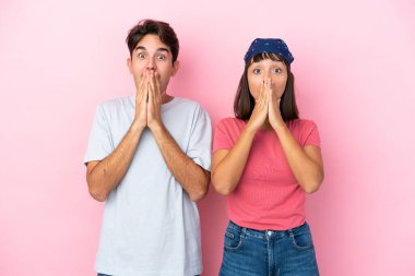 Pembe arka planda izole edilmiş genç bir çift ağzını kapatırken gülümsüyor.