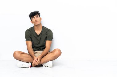 Genç Arjantinli adam yerde oturuyor ve yukarı bakıyor.