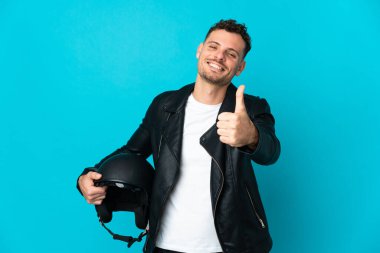 Motosiklet kasklı beyaz adam mavi arka planda izole edildi. Başparmakları havada çünkü iyi bir şey oldu.