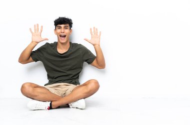 Genç Arjantinli adam yerde oturmuş parmaklarıyla 10 'a kadar sayıyor.