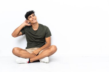 Genç Arjantinli bir adam yerde oturmuş bir fikir düşünüyor.