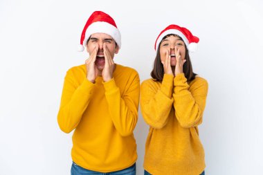 Genç melez çift Noel 'i beyaz arka planda izole bir şekilde kutluyor bağırıyor ve bir şeyler duyuruyorlar.