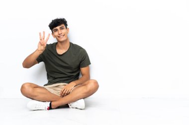 Yerde oturan genç Arjantinli adam mutlu ve parmaklarıyla üçe kadar sayıyor.