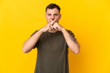 Sarı arka planda izole edilmiş beyaz yakışıklı genç bir adam sessizlik işareti gösteriyor.