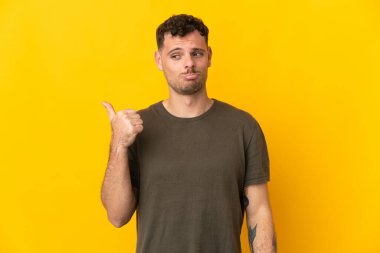 Sarı arka planda izole edilmiş genç beyaz yakışıklı adam mutsuz ve bir tarafı işaret ediyor.