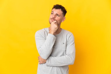 Beyaz tenli yakışıklı adam sarı arka planda izole edilmiş bir şekilde yukarı bakarken bir fikir düşünüyor.