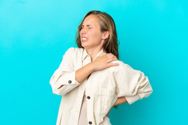 Genç, beyaz bir kadın mavi arka planda izole edilmiş. Omuz ağrısı çekiyor. Çabaladığı için.