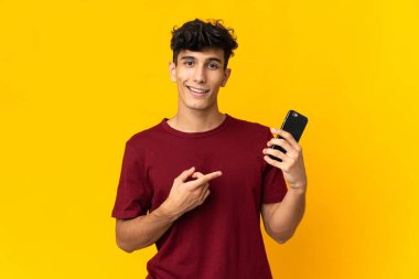 Arjantinli genç adam sarı arka planda cep telefonu kullanarak izole edilmiş.