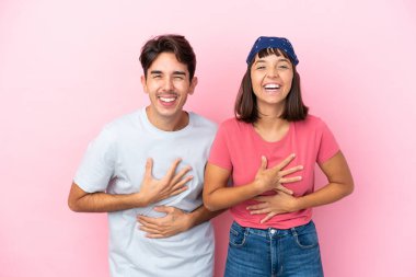 Pembe arka planda yalnız yaşayan genç çift ellerini göğsüne koyup gülümsüyor.