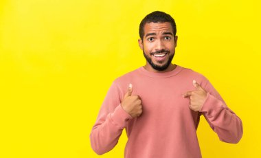 Sarı arka planda, şaşırtıcı bir yüz ifadesi olan genç Latin bir adam.