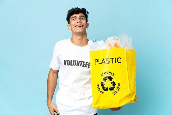 Young Argentinian man holding a bag full of plastic laughing