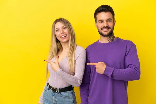 両側に指を指して製品を提示孤立黄色の背景に若いカップル — ストック写真