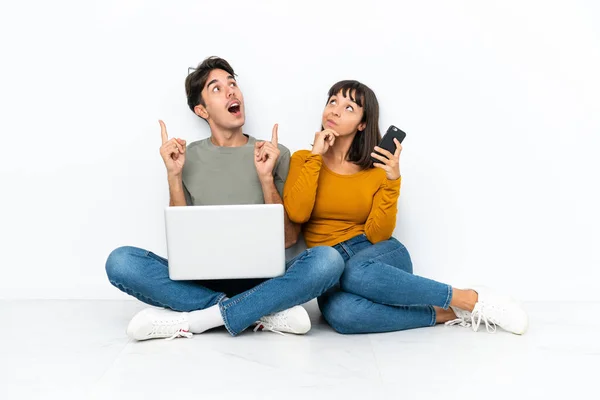 年轻的一对夫妇 带着笔记本电脑和手机坐在地板上 一边想办法一边挠头 — 图库照片