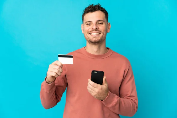 Νεαρός Καυκάσιος Όμορφος Άνδρας Απομονωμένος Μπλε Φόντο Αγοράζει Κινητό Πιστωτική — Φωτογραφία Αρχείου