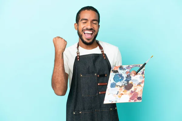 Ung Konstnär Latin Man Håller Palett Isolerad Blå Bakgrund Firar — Stockfoto