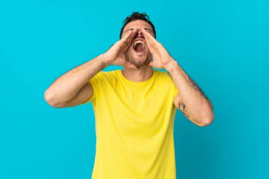 Beyaz tenli yakışıklı adam mavi arka planda izole edilmiş bağırıyor ve bir şeyler söylüyor.