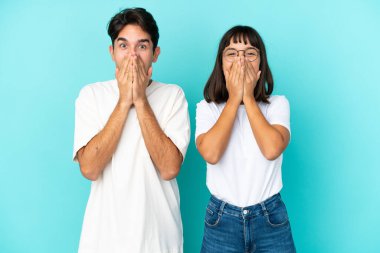 Genç melez çift mavi arka planda izole edilmiş, ağzı kapalıyken gülümsüyor.