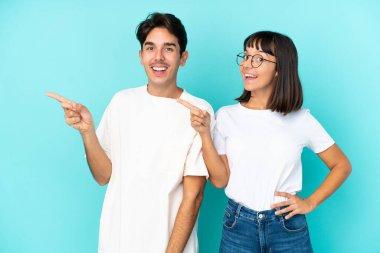 Mavi arka planda izole edilmiş genç ve melez bir çift parmak göstererek bir ürün sunuyor.