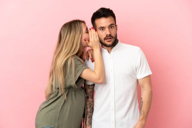 Hamile kadın ve erkek izole pembe arka planda bir şeyler fısıldıyor.