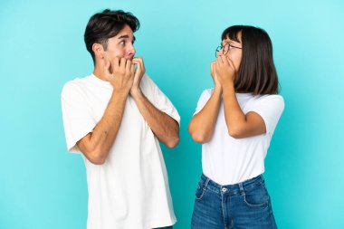 Mavi arka planda soyutlanmış genç melez bir çift ellerini masaya koymaktan korkuyor ve biraz gergin.