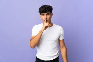 Arjantinli genç bir adam arka planda izole edilmiş. Parmağını ağzına koyduğunda sessizlik işareti gösteriyor.