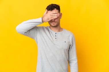 Beyaz tenli yakışıklı adam sarı arka planda izole edilmiş gözlerini elleriyle kapatıyor. Bir şey görmek istemiyorum.