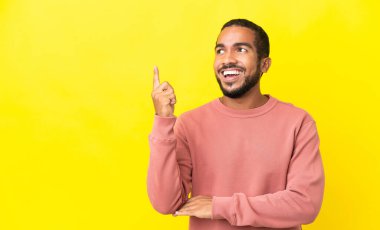 Sarı arka planda izole edilmiş genç latin adam harika bir fikre işaret ediyor.