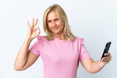 Beyaz arkaplanda izole edilmiş cep telefonu kullanan orta yaş parmaklarıyla tamam işareti gösterir