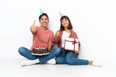 Genç melez çift, beyaz arka planda izole bir şekilde yerde oturmuş doğum gününü kutluyorlar. Çünkü iyi bir şey oldu.