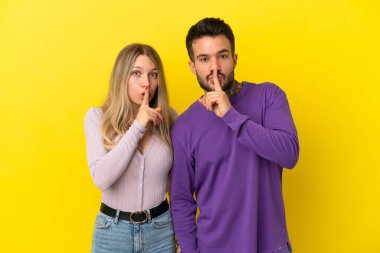 İzole edilmiş sarı arka planda genç bir çift ağzını kapatma ve sessizlik işareti gösteriyor.