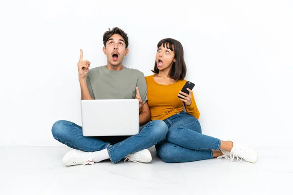 一对年轻的夫妇 带着笔记本电脑和手机坐在地板上 想着用手指指指 — 图库照片