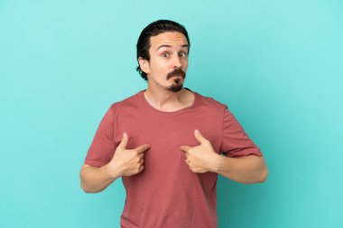 Mavi arka planda izole edilmiş genç beyaz adam kendini işaret ediyor.