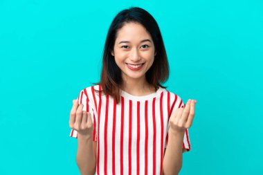 Genç Vietnamlı kadın mavi arka planda izole edilmiş para hareketi yapıyor.