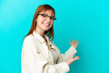 Kızıl saçlı kız mavi arka planda gözlüklü ve bir şeyler sunan