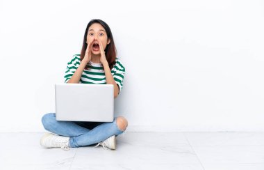 Yerde dizüstü bilgisayarı olan genç Vietnamlı kadın beyaz duvarda izole bir şekilde oturmuş bağırıyor ve bir şey duyuruyor.