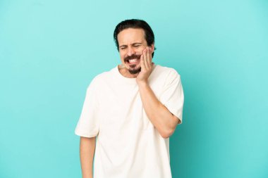 Mavi arka planda diş ağrısı olan genç beyaz bir adam izole edilmiş.