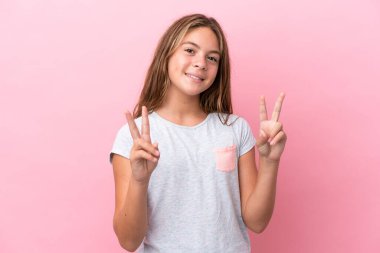 Pembe arka planda izole edilmiş küçük beyaz kız iki eliyle zafer işareti gösteriyor.