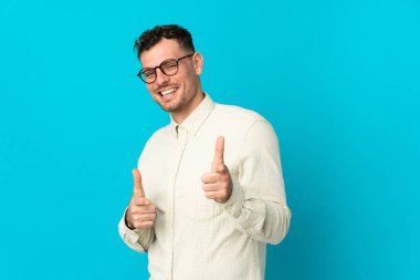 Genç, beyaz, yakışıklı, mavi arka planda soyutlanmış ve gülümseyen bir adam.