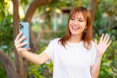 Açık havada cep telefonu kullanan güzel, kızıl saçlı bir kadın.
