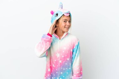 Beyaz arka planda izole edilmiş tek boynuzlu pijamalı küçük bir kız kulağına elini sürerek bir şeyler dinliyor.