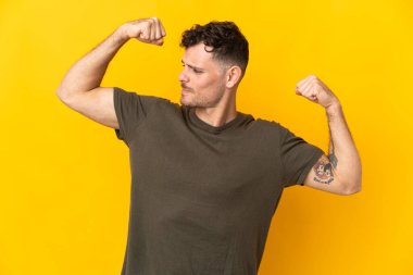 Sarı arka planda izole edilmiş beyaz, yakışıklı genç adam güçlü bir jest yapıyor.