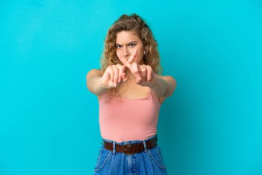 Mavi arka planda izole edilmiş genç sarışın kadın bir hareketi durdurmak için eliyle hareket yapıyor.