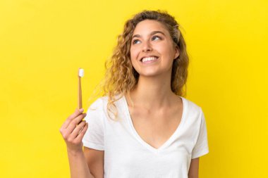 Beyaz dişlerini fırçalayan genç bir kadın sarı arka planda izole edilmiş bir şekilde yukarı bakarken bir fikir düşünüyor.