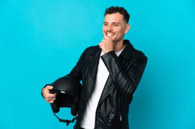 Mavi arka planda izole edilmiş motosiklet kasklı beyaz adam yan tarafa bakıyor ve gülümsüyor.