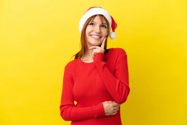 红头发姑娘头戴一顶黄色背景的圣诞帽 抬头一看就想出了个主意 — 图库照片