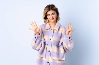 Mavi arka planda izole edilmiş genç Rus kadın parmaklarıyla dokuz sayıyor.