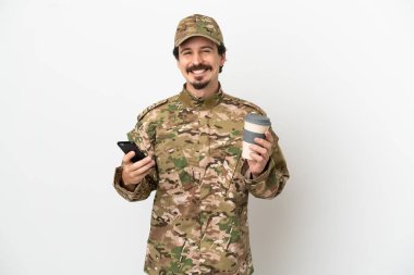 Beyaz arka planda izole edilmiş bir asker elinde kahve ve bir cep telefonu tutuyor.